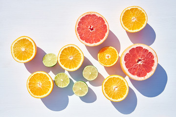 Ripe orange, grapefruit and lime halves on white wooden background, shot from above in harsh sunlight with long colored shadows.