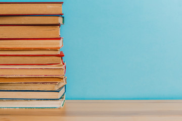A simple composition of many hardback books, raw books on a wooden table and a bright blue background. Going back to school. Copy space. Education.