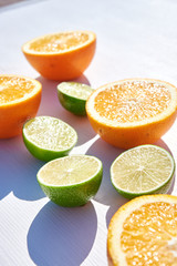 Ripe orange and lime halves packed on white wooden background, vertical close-up shot in harsh sunlight with long colored shadows. Diagonal composition.