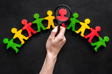 Wooden figures of people under black magnifying glass on black background. Recruitment, hiring,...