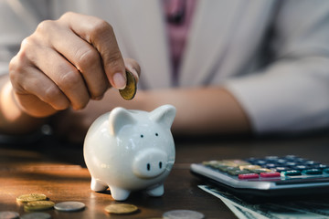 Closeup of business woman hand putting money coin into piggy bank for saving money. saving money...