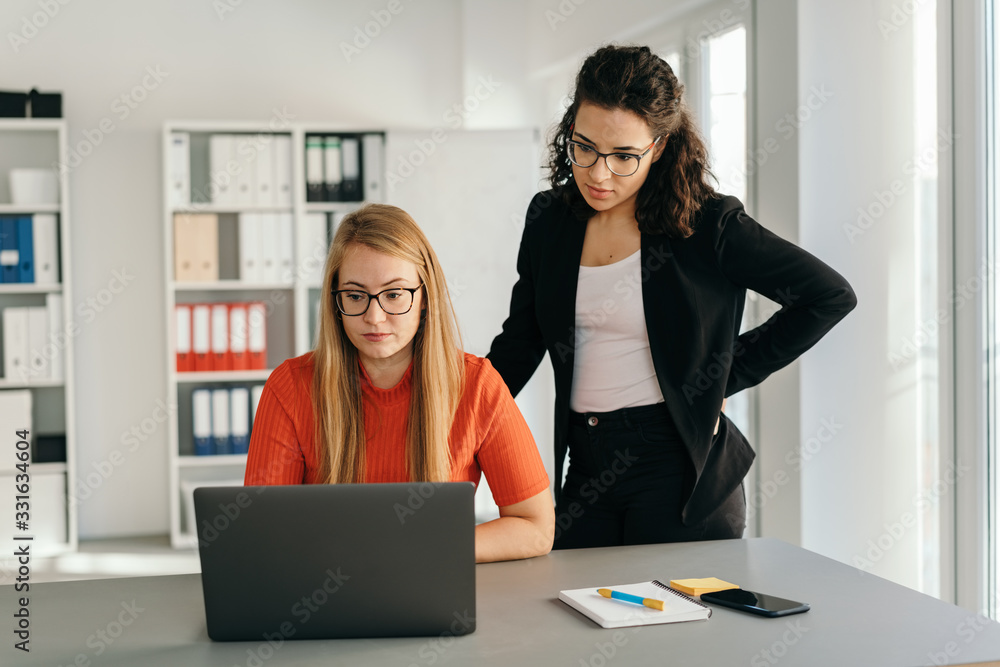 Wall mural two serious young businesswomen reading a laptop