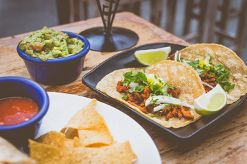 Al Pastor Tacos with roasted pork, spring onions and lemon wedges on the side, with tortilla chips and guacamole
