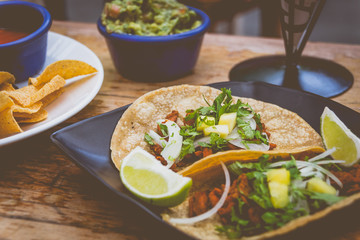 Al Pastor Tacos with roasted pork, spring onions and lemon wedges on the side, with tortilla chips and guacamole