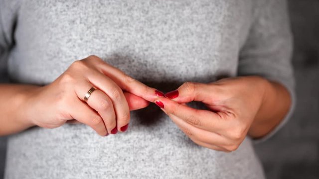 Nervous woman picks at her red nails. Close up of woman's hands picking her nails. Female strips red nail polish off her nails with her fingers from stress.