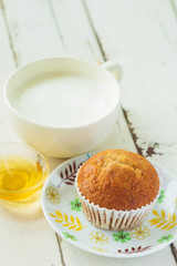 Close up banana cake on white plate with honey and cup of milk on wooden table.