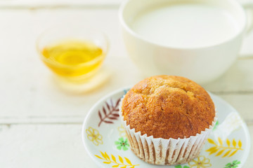 Close up banana cake on white plate with honey and cup of milk on wooden table.