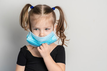 Portrait of a little girl of European appearance in a disposable mask with two ponytails. girl...