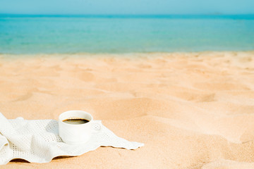 coffee espresso cup with ocean , beach and seascape. Blue sky, white sand, woven zonik, wooden beach chair. Sea vacations. The concept of travel, rest and relaxation.