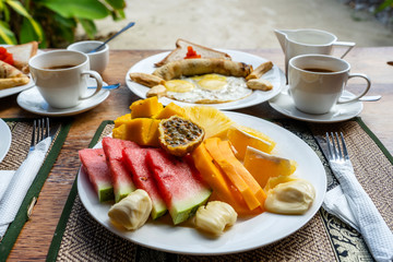 Tropical breakfast of fruit, coffee and scrambled eggs and banana pancake for two on the beach near sea