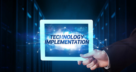 Young business person working on tablet and shows the inscription: TECHNOLOGY IMPLEMENTATION