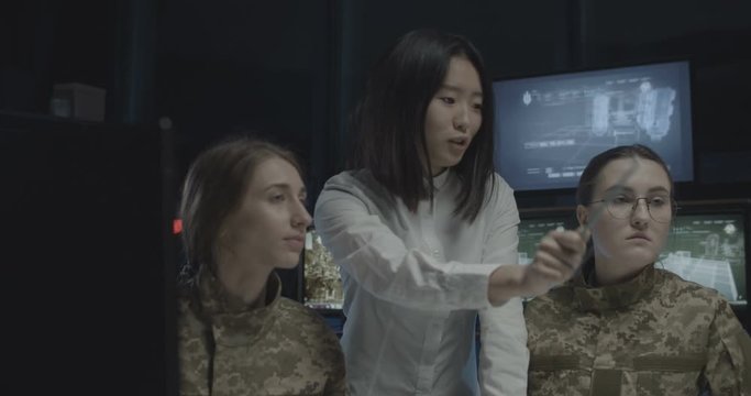 Young Asian woman giving tasks to two Caucasian female soldiers in troops operation center. Women officers studying some data and information of army under supervision of teacher.