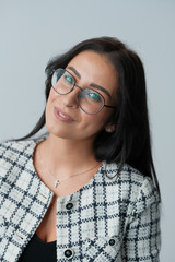 Portrait of a smiling mid-aged business woman with dark hair and brown eyes in glasses and a jacket against a light wall