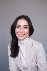 Obraz premium Portrait of a smiling mid-aged business woman in a light milk-colored trouser suit and turtleneck against a light wall.