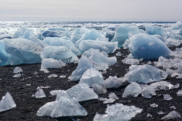 The block of ice is lying on the black volcanic sand on the 