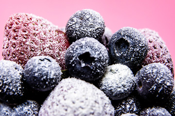 Macro view of frozen berries: strawberry, blueberry on pink background