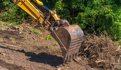 Yellow backhoe with hydraulic piston arm. Heavy machine for excavation in construction site.
