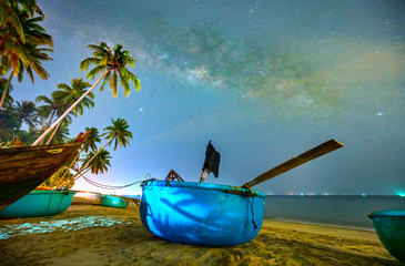 Midnight landscape with basket boat, coconut palm tree Silhouette and Milky Way in the sky on a beautiful summer night. Long exposure photograph.