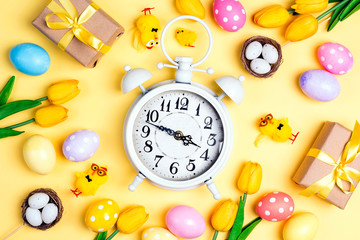 Easter alarm clock with colorful eggs and tulips on yellow background.