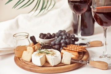 Two glass of red wine and plate with assorted cheese, fruit and other snacks for party