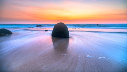 Dawn on beautiful beache with waves crashing on the shore creating silk-like streaks of different shapes piercing the rock. It was great and impressive to watch the sunrise here - obrazy, fototapety, plakaty