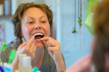 Woman flossing her teeth in a bathroom mirror