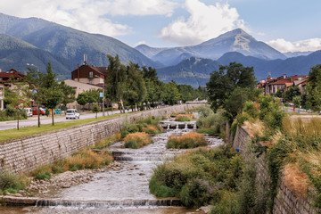 Fototapeta premium View of Bansko town, bulgarian ski resort in summer, Pirin Mountains in the background, a river in the foreground, Bulgaria.