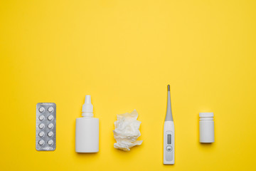 Pills, medical thermometer, nose spray and tissue. Different medications on yellow background. Cold...