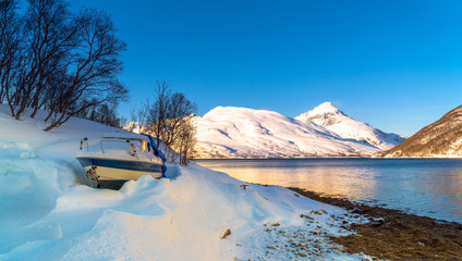 Kaldfjord, Troms og Finnmark / Norway - March 4th, 2020: Small recreational boat buried in the snow on the banks of a fjord in the Arctic Ocean