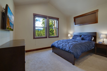 Beautiful large new bedroom with queen size bed with blue blanket and bege walls. Natural setting, vaulted ceiling,