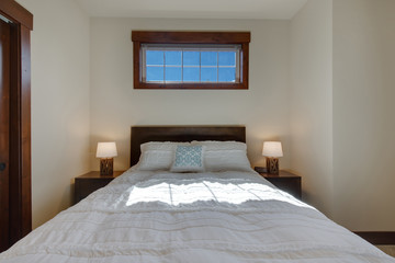 Bright new natural tones bedroom with queen size bed with grey carpet and three windows, one long above the bed. Tv on the wall. and rich wooden doors.