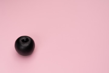 Matte black apple on the pink background. The object is at the left side of the picture. Minimal style. Conceptual minimalism. Matte surface. Fruit. One. Copy space