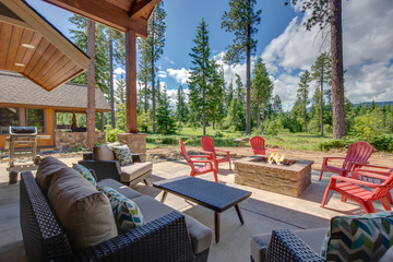 Back yard with fire pit and red chairs near newly bild luxury real estate home with forest biew and green grass.