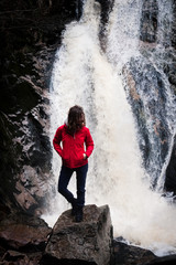 Frau steht von der Kamera abgewandt von der Kamera und schaut seitlich auf den Wasserfall