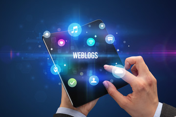 Businessman holding a foldable smartphone with WEBLOGS inscription, social media concept