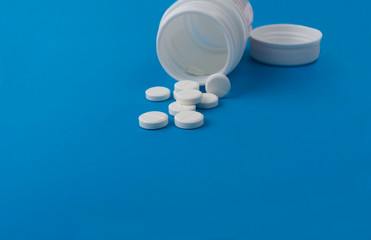 white tablets in a plastic jar with a lid, lying on an isolated blue background