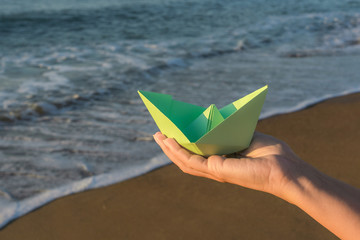 Closeup view photography of young kid hand holding green folded paper boat in hand isolated at...