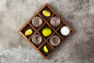 Tequila shots, limes and salt on wooden board on grey background
