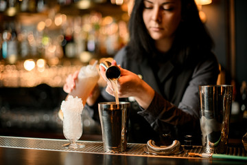 brunette barman gently pours the drink into steel shaker using beaker