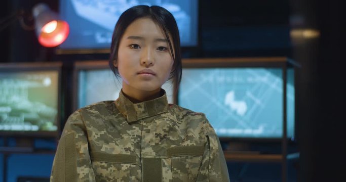 Portrait of pretty Asian female soldier standing in monitoring room and looking staright at camera. Attractive woman in militarian uniform working in troops. Girl in army concept.