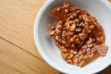 Peanut brittle pieces on a white bowl on wooden table