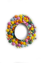 Cookie cutter in shape of a easter egg on a bunch of colorful chocolate candies isolated on white background. Easter background
