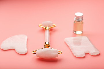 Gua sha massage tool made of natural pink Quartz-roller, jade stone and oil, on a pink background for face and body care. Part of traditional Chinese medicine