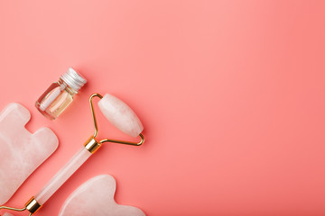 A set of tools for face Massage technique Gua Sha made of natural rose quartz on a pink background. Roller, jade stone and oil in a glass jar for face and body care.