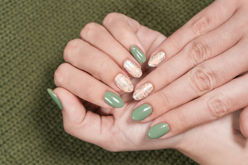 Obraz na płótnie Canvas Closeup top view of two beautiful female hands of white woman with fresh modern stylish manicure of green and beige pastel colors. Hands isolated on green knitted texture background. 