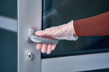 Person in transparent rubber protective gloves holding door handle during flu covid virus outbreak, coronavirus epidemic and infectious diseases