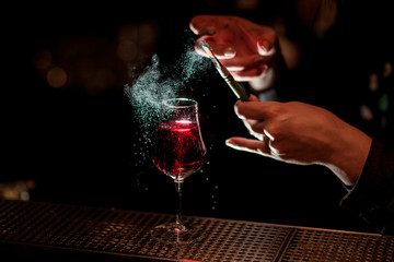 barman's hand professionally decorates alcoholic cocktail with colored powder using brush.