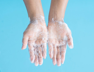 Closeup woman's hand washing with soap on blue background, health care concept