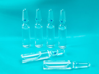 Glass ampoules with medicine on a blue background. The rear row of ampoules stands in the row, with two pieces lying in the foreground. The place for an inscription