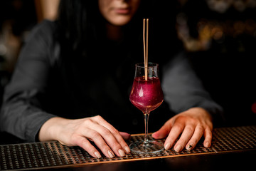 Close-up wineglass with cocktail which decorated by two sticks stand on bar.